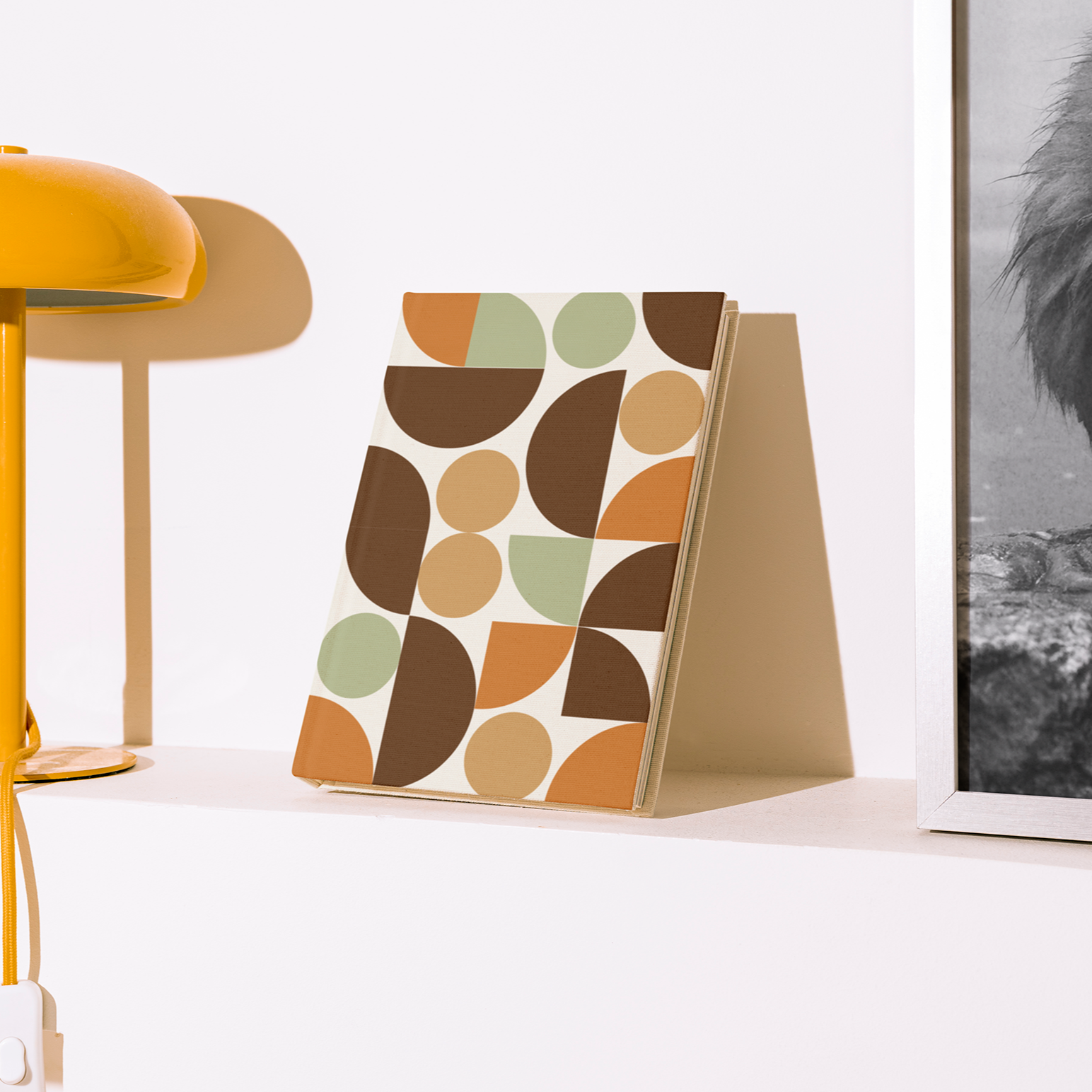 Yellow lamp and decorative book on a white surface with a framed black and white photo in the background.